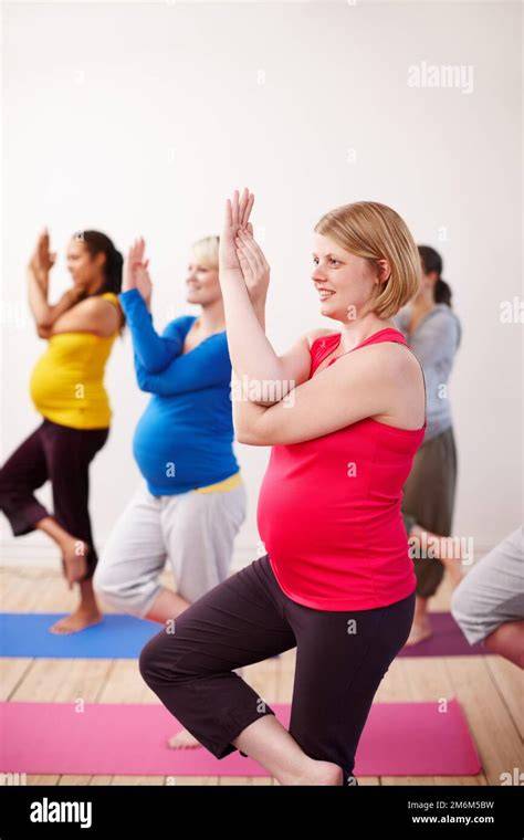 Eine Gruppe von schwangeren Frauen, die entspannt und lächelnd an einer Yoga-Stunde teilnehmen.