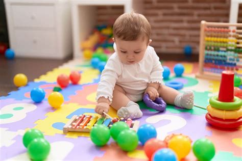 Baby im 10. Monat sitzt auf einer Krabbeldecke und greift nach einem Spielzeug.