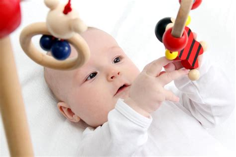 Eine Nahaufnahme eines hölzernen Spielbogens, bei dem ein Baby nach bunten Holzfiguren greift.