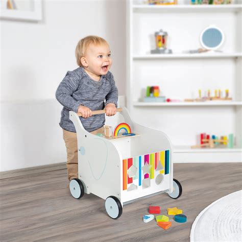Ein Kind schiebt einen hölzernen Lauflernwagen und lächelt dabei.