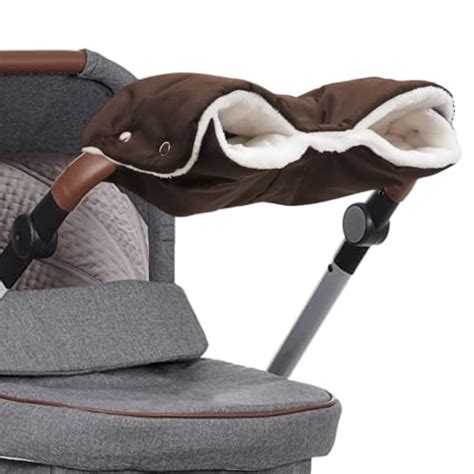 Ein Paar Hände, die in einem Lammfell-Kinderwagen-Handwärmer am Schiebegriff eines Kinderwagens stecken, mit verschneiter Landschaft im Hintergrund.
