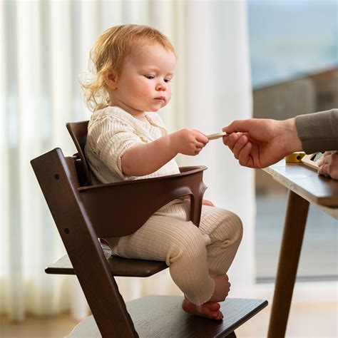 Ein Baby sitzt auf einem Hochstuhl und greift nach einem Stück Gemüse