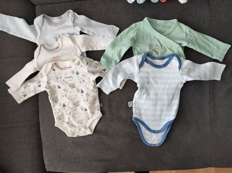 Übersicht verschiedener Babykleidungsstücke wie Bodys, Hosen und Mützen