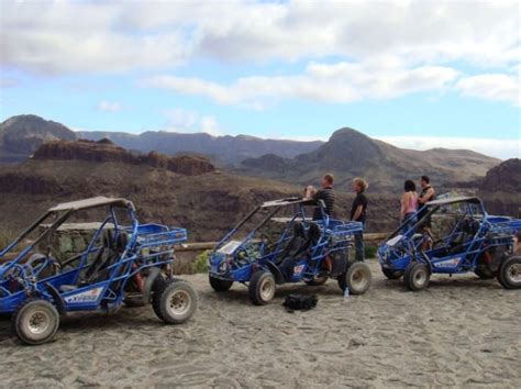 Panoramablick auf die bergige Landschaft Gran Canarias mit einem Buggy auf einem Schotterweg.