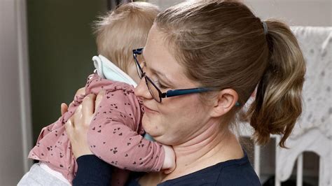 Eine Szene, in der eine Mutter ihr Baby auf dem Arm hält und es einer freundlich lächelnden Großmutter aus sicherer Entfernung beobachtet.