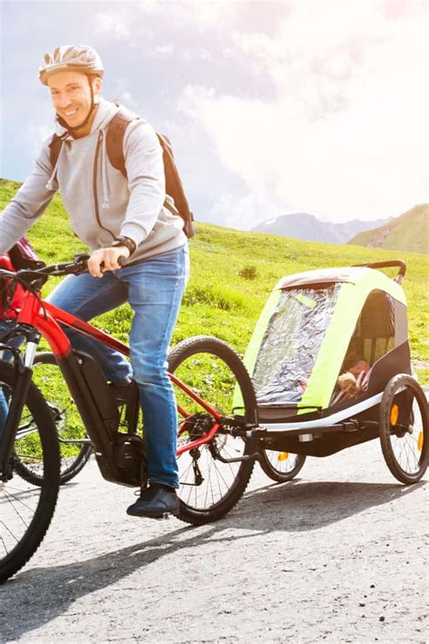 Ein Fahrradanhänger mit Kindern, der auf einem breiten Waldweg fährt