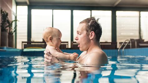 Eltern halten ihr Baby im Wasser, beide lächeln.