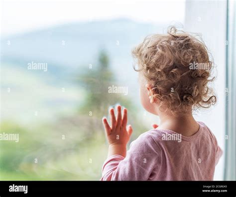 Eine Frau blickt nachdenklich aus dem Fenster, im Hintergrund verschwommen ein Kinderzimmer.